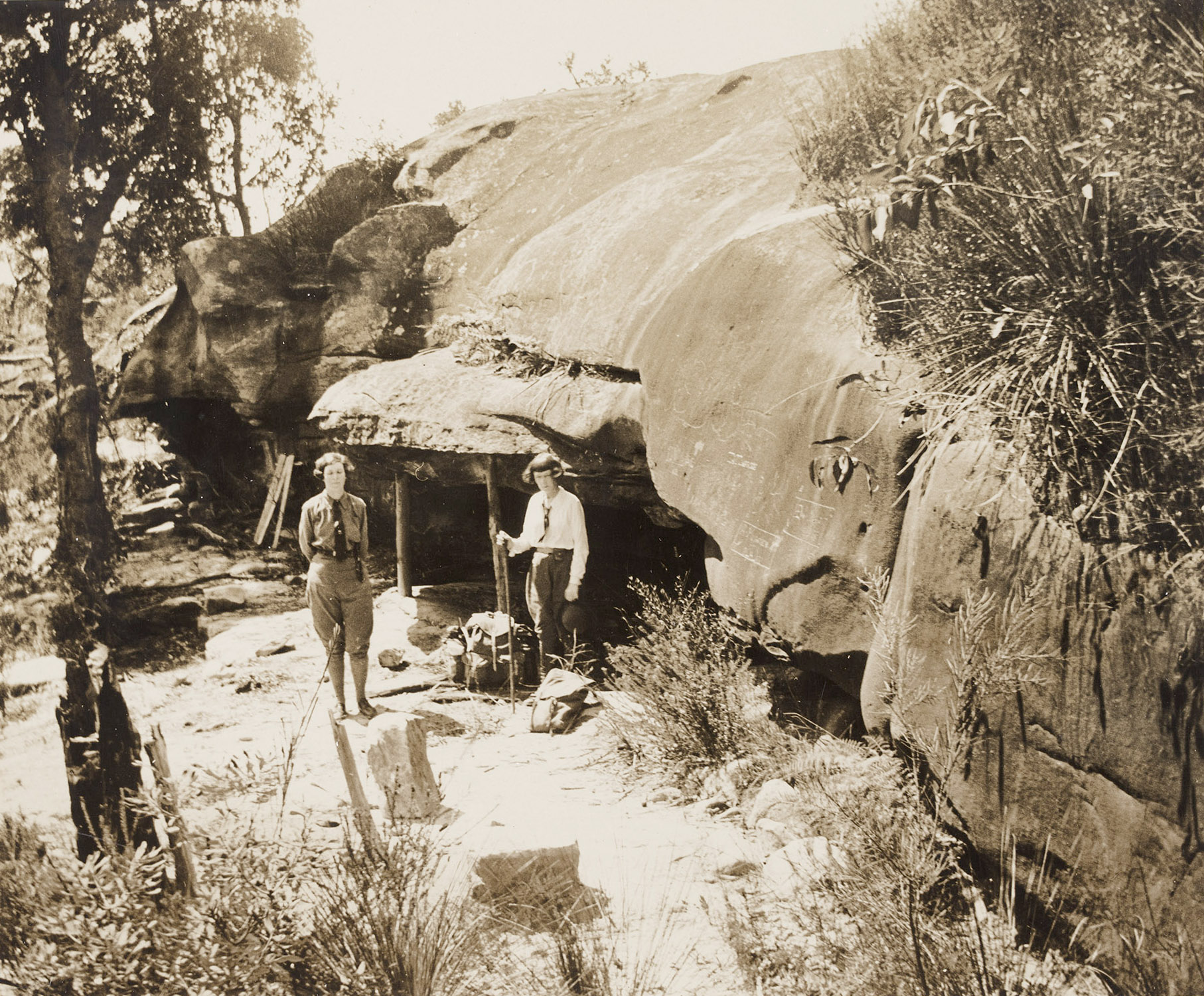 two women stand outside a cave in a rock face