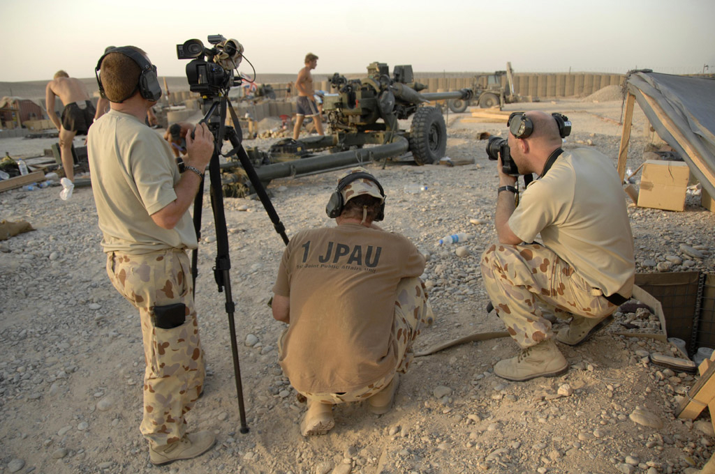 A group of people in army fatigues with cameras in a desert area