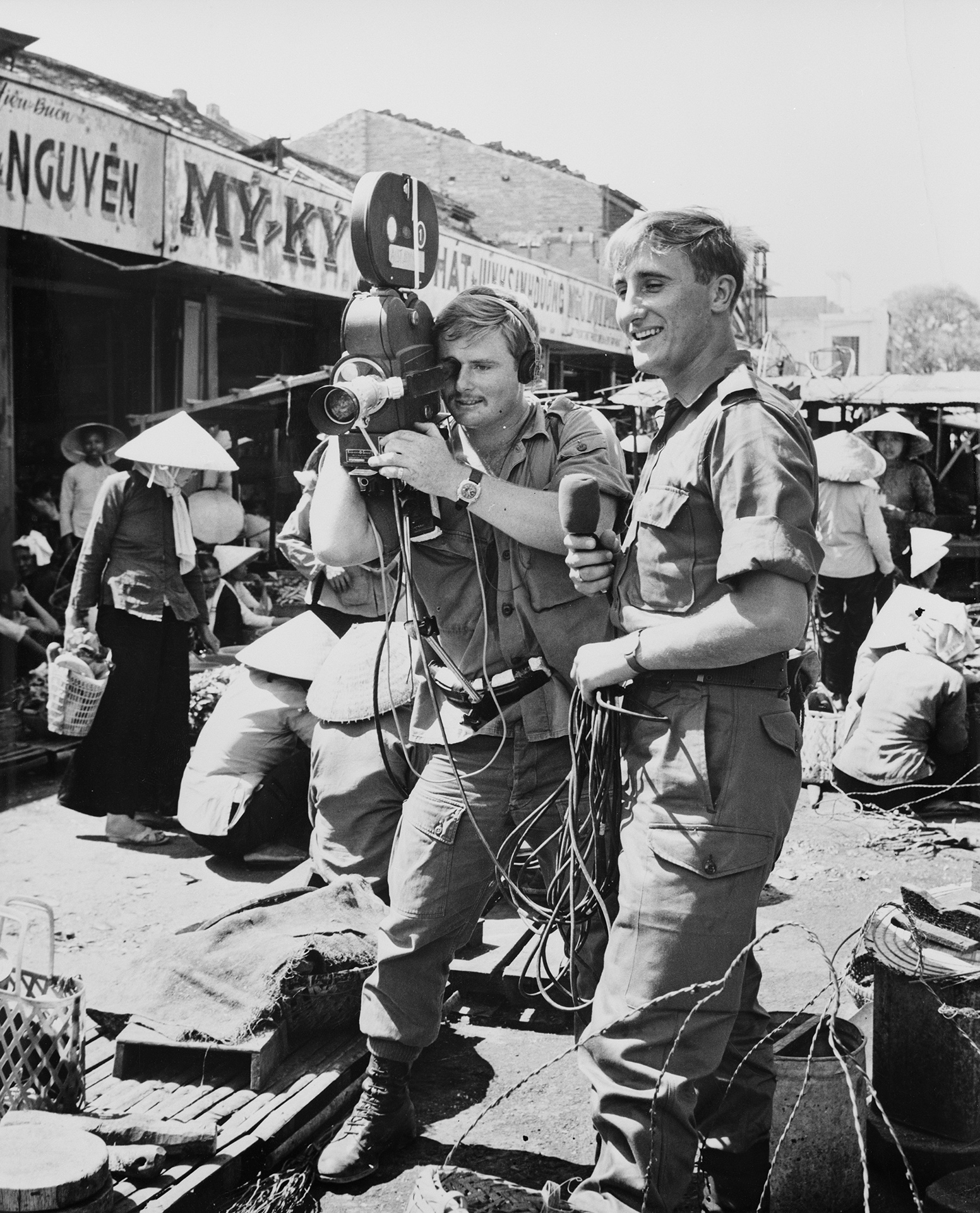 Black and white photograph of man with moving picture camera and another man with a microphone