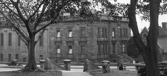 Black and white photo of large school behind trees