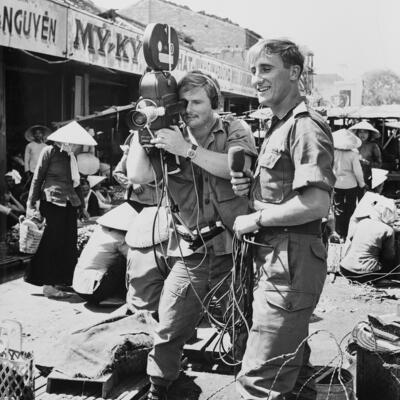 Black and white photograph of man with moving picture camera and another man with a microphone