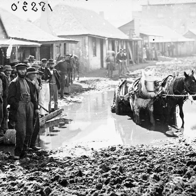 Horse and cart struggling through muddy street as men watch