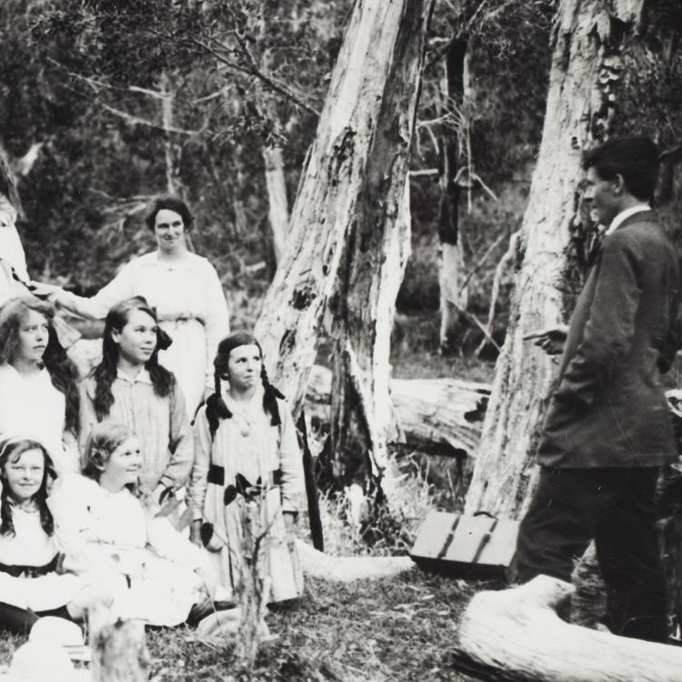 Chisholm addressing a class of smiling schoolgirls in the bush