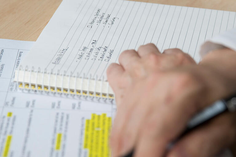 Man's hands holding pen with notebook open on desk