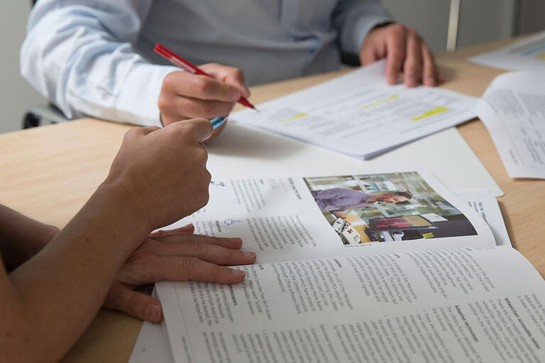 close up of peoples' hands with papers, books and pens at a desk