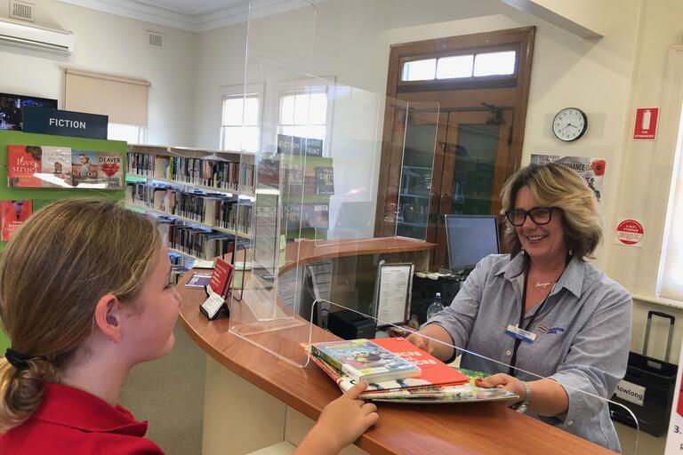 Woman at library service desk handing books to a girl