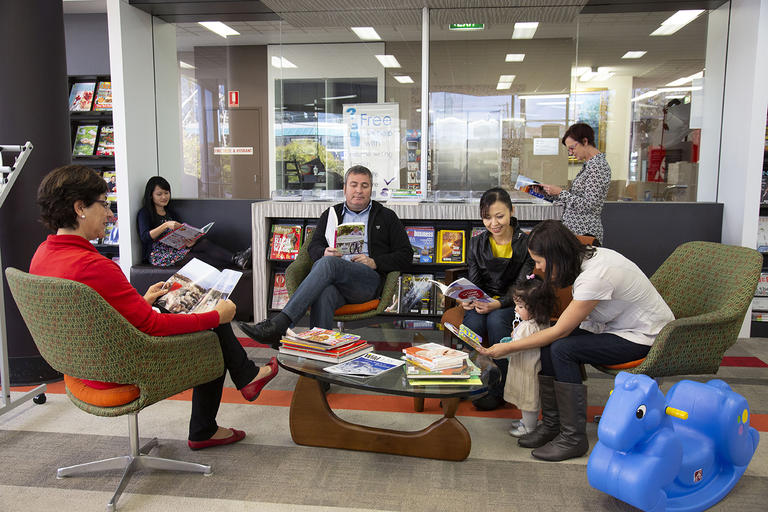 A number of people sitting in a library space reading