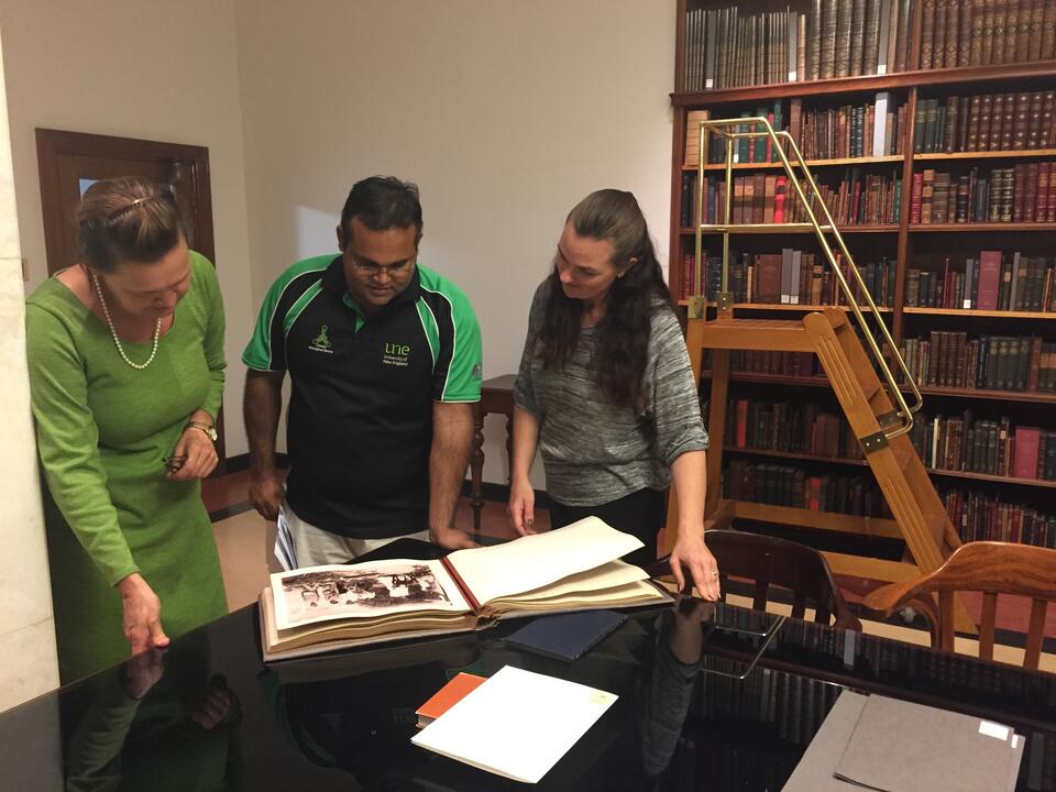 a group two women and a man looking at a manuscript on a table