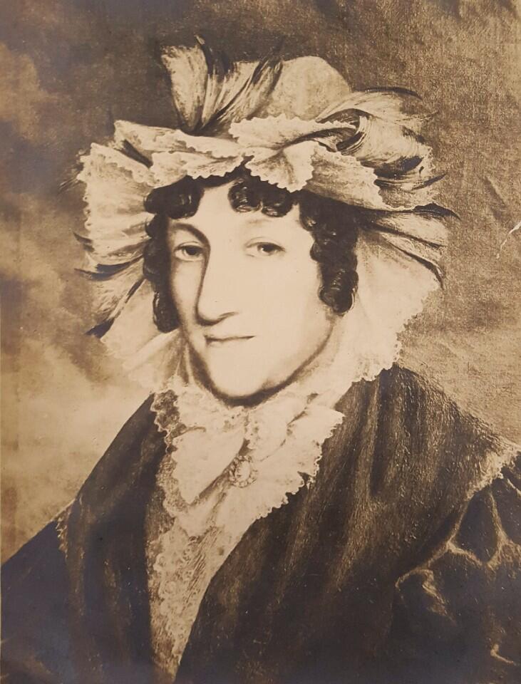 A portrait of a woman wearing a very ruffled bonnet, ruffled blouse and coat.