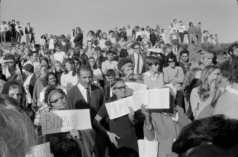 A large crowd of Aboriginal rights protesters holding signs at a beach.