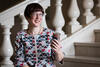 Dr Lisa Murray - wearing a red, white and blue dress - is sitting on the marble steps of the Mitchell Vestibule.